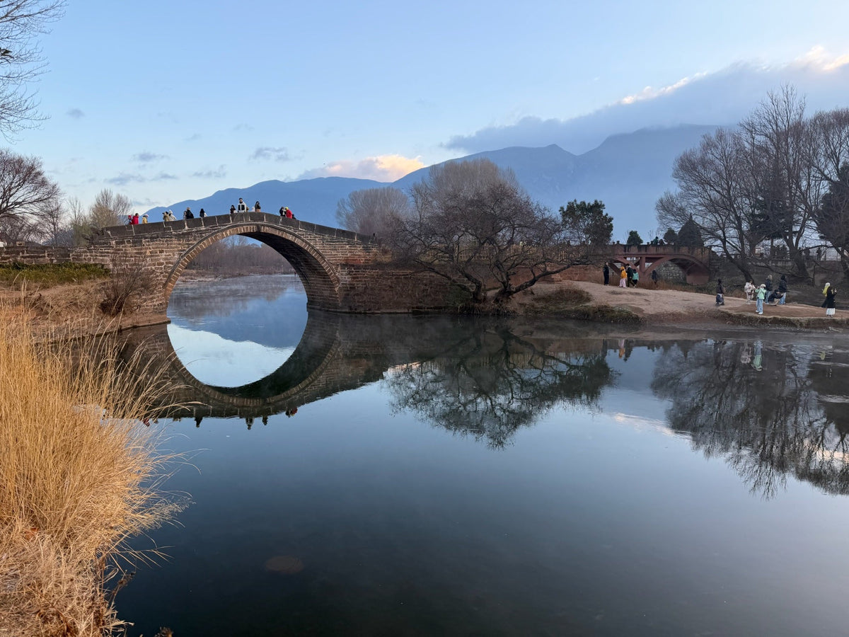 Yujin Bridge in Shaxi, Yunnan, on a winter morning, with bare trees reflected in the river